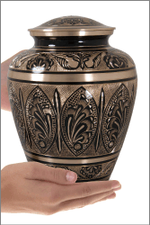 ornate etched black and brass cremation urn shown in hands for size scale